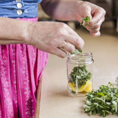 Jemand zupft Majoran in ein Glas.