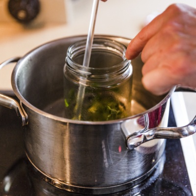 Jemand erwärmt ein Glas mit Bio-Majoran im Wasserbad.