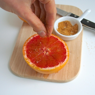 Jemand streut braunen Zucker über eine Bio-Grapefruit.