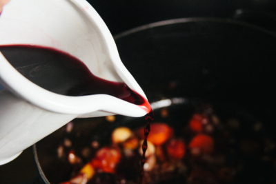 Jemand schüttet Rotwein in einen Topf mit Bio-Würstel-Gulasch.