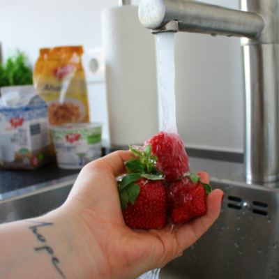 Jemand wäscht Bio Erdbeeren unter fließendem Wasser.
