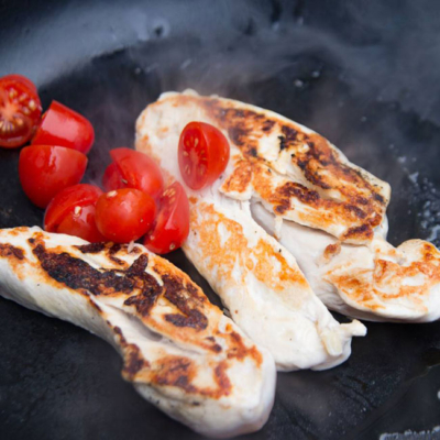 Gebratenes Hühnerfleisch und Bio-Paradeiser in einer Pfanne.
