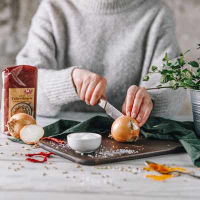 Jemand halbiert eine Zwiebel, daneben eine Packung Ja! Natürlich Bio-Tellerlinsen.