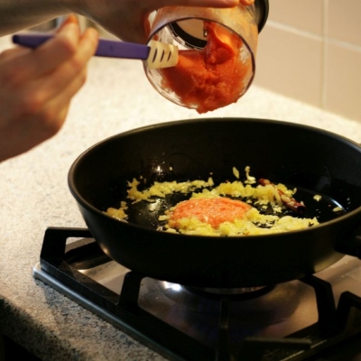 Jemand gibt Würz-Püree in eine Pfanne mit angebratenem Bio-Zwiebel.