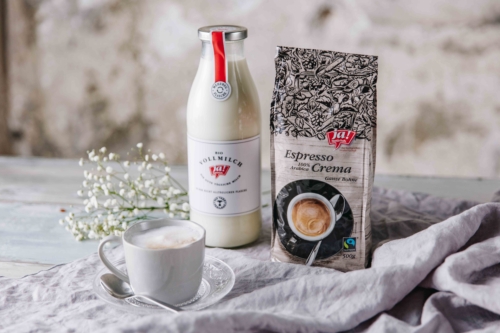 Eine Tasse Kaffee und eine Packung Ja! Natürlich Bio-Espresso Crema und eine Flasche Vollmilch.