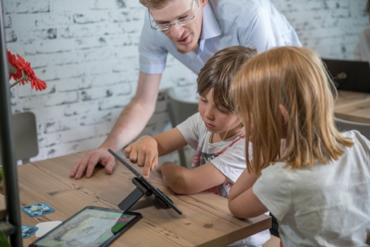 Ein Vater, der mit seinen Kindern etwas auf dem iPad anschaut.