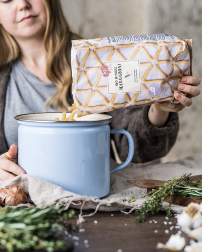 Jemand schüttet Ja! Natürlich Bio-Makkaroni in einen Topf.