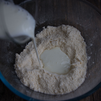 Jemand schüttet Bio-Milch in die Schüssel mit Mehl.
