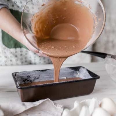 Jemand gießt den Schokoteig in eine Backform.