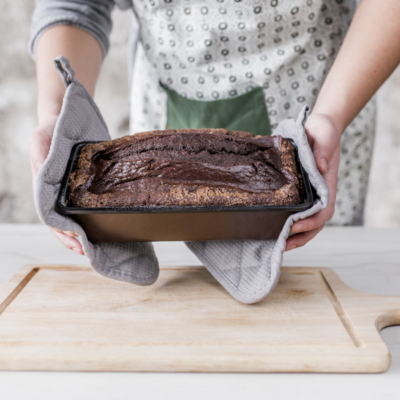 Eine Person hält einen Bio-Schokokuchen mit Ofenhandschuhen in einer Backform.