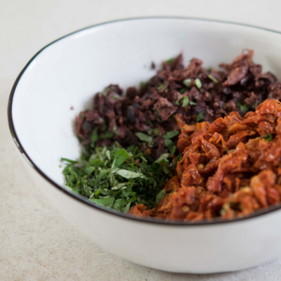 Fein gehackte Bio-Oliven, getrocknete Paradeiser und Kräuter in einer Schüssel.