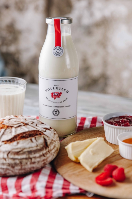 Eine Flasche Ja! Natürlich Bio-Vollmilch neben einem Brett mit Brot, Butter und Marmelade.
