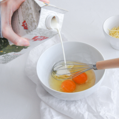 Jemand schüttet Ja! Natürlich Bio-Milch in eine Schüssel mit Eiern.