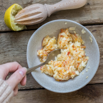 Jemand mischt geriebenen Bio-Apfel mit Zitronensaft in einer Schüssel.