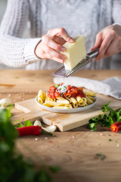 Eine Person reibt Bio-Parmesan über Penne all’arrabbiata.