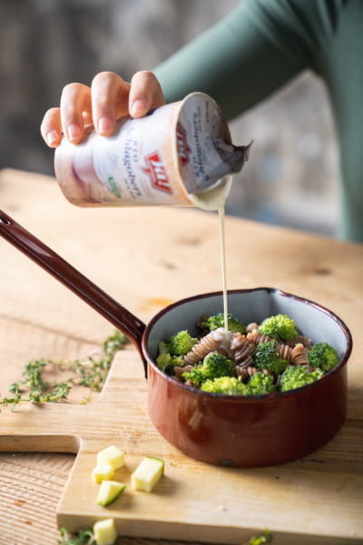 Ja! Natürlich Bio-Schlagobers wird in einen Topf Pasta und Brokkoli gegossen.