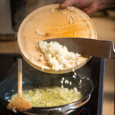 Jemand gibt Bio-Zwiebel in eine Pfanne.