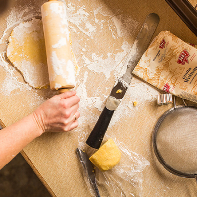 Jemand rollt den Teig mit einer Nudelwalze aus.