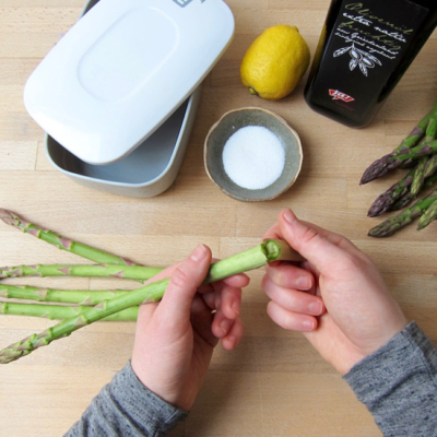 Jemand bricht die Enden von Spargel ab, daneben eine Flasche Ja! Natürlich Bio-Olivenöl.
