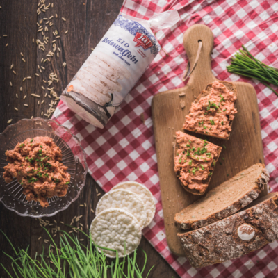 Ein Brot mit Reiswaffelaufstrich auf einem Brett, daneben eine Packung Ja! Natürlich Bio-Reiswaffeln mit Salz.