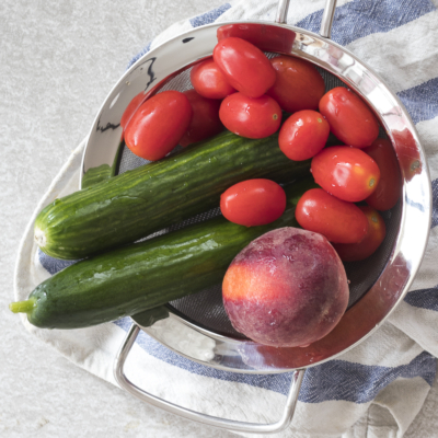 Eine Schüssel mit Bio-Gurken, Paradeisern und Pfirsich.