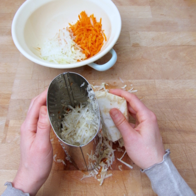 Jemand raspelt Bio-Gemüse mit einer Reibe.