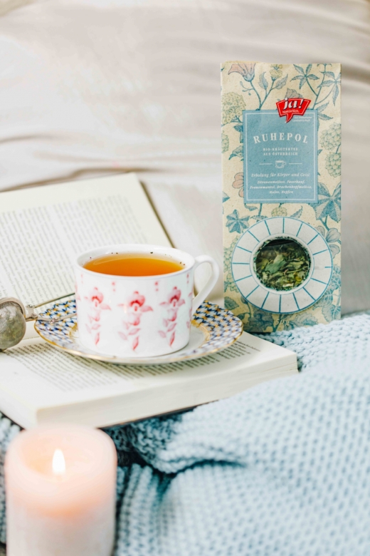 Auf einer Decke liegt ein Buch und eine Tasse Ja! Natürlich Bio-Ruhepool Tee.