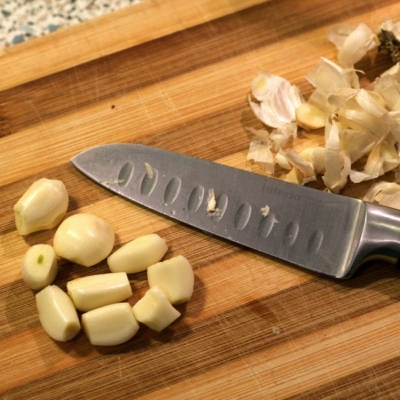 Geschälte Bio-Knoblauchzehen neben einem Messer.