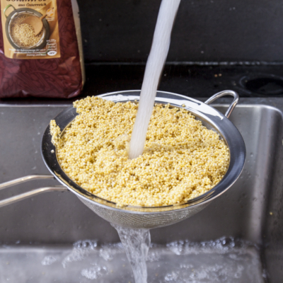 Jemand wäscht Bio-Hirse in einem Sieb ab.