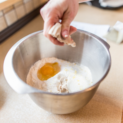 Jemand bröckelt Bio-Hefe in eine Schüssel mit Mehl und einem Ei.