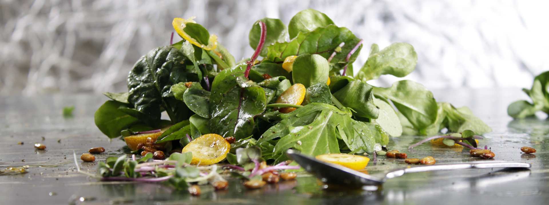 Blattsalatmix mit gelben Tomaten liegt auf einer Platte mit einem Löffel davor