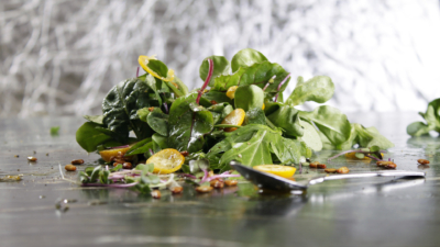 Blattsalatmix mit gelben Tomaten liegt auf einer Platte mit einem Löffel davor