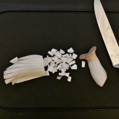 Ganze und in Würfel geschnittene Kräuterseitlinge auf einem Brett.