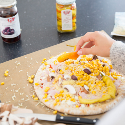 Jemand belegt eine Pizza mit Zutaten von Ja! Natürlich.