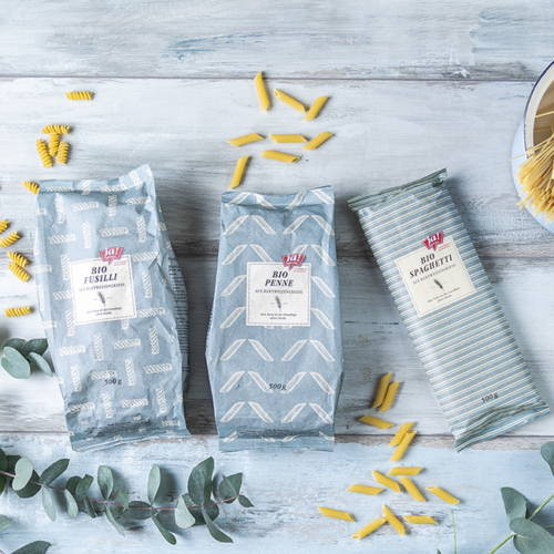 Bio-Fusilli, Bio-Penne und Bio-Spaghetti in einer Papierverpackung von Ja! Natürlich liegen auf einem Tisch