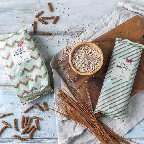 Bio Vollkorn Spaghetti und Bio-Vollkorn Spiralen in Papierverpackung von Ja! Natürlich liegen auf einem dunklen Brett