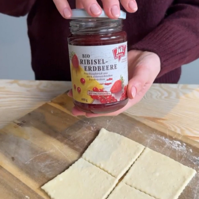 Teig ausgerollt auf einem Brett und ein Marmeladeglas wird aufgeschraubt