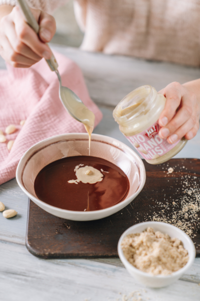 Jemand gibt Bio-Mandelmus in eine Schüssel mit Schokolade.