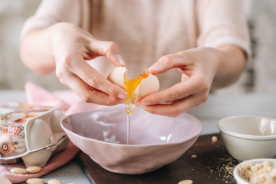 Jemand schlägt ein Bio-Ei über einer Schüssel auf.
