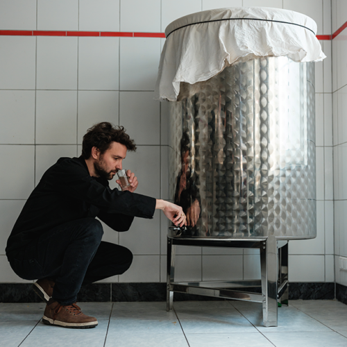 Mann steht bei Kombucha-Tank und entnimmt eine Probe.