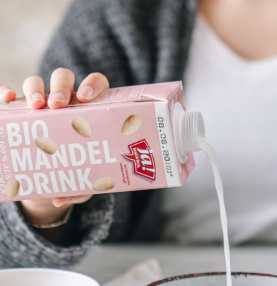 Jemand schüttet den Ja! Natürlich Bio-Mandeldrink in eine Schüssel.