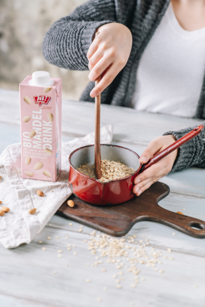 Jemand rührt Ja! Natürlich Bio-Haferdrink in einen Topf mit Haferflocken.