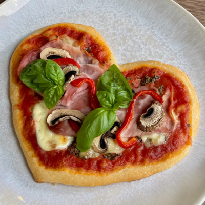 Fertige Herzpizza mit Schinken, Pilzen und Basilikum