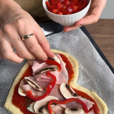 Pizza wird mit Paprika, Pilzen und Schinken belegt