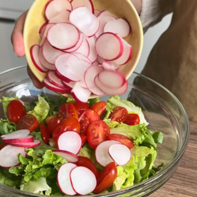 Radieschen werden in eine Schale mit Salat und Tomaten gegeben
