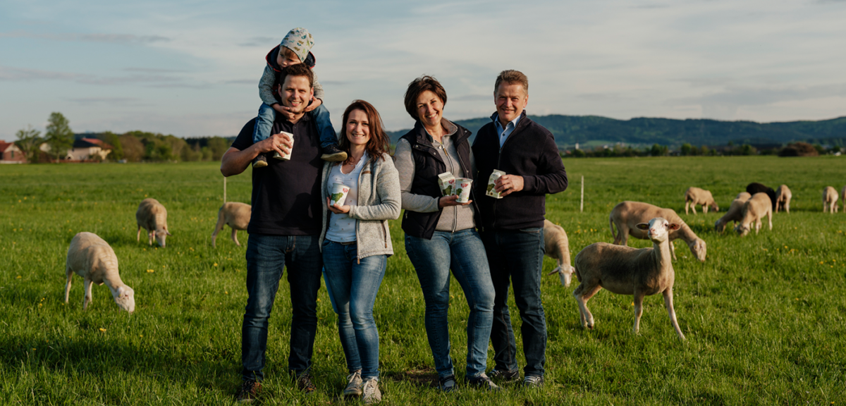Familie Stangl (5 Personen) steht auf der Weide. Im Hintergrund grasen die Schafe