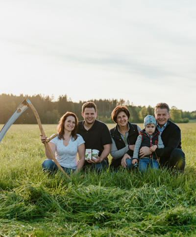 Familie Stangl kniet auf der Weide mit der Sense und Schafmilch-Produkten