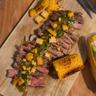 Fertiges Steak getoppt mit Chimichurri und Mais auf einem Brett