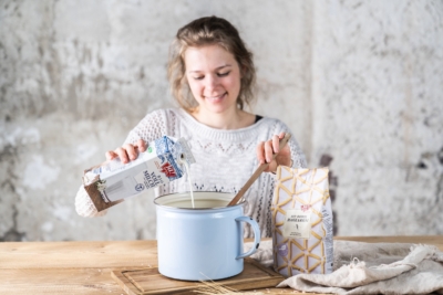 Jemand schüttet Ja! Natürlich Bio-Vollmilch in einen Topf, daneben eine Packung Ja! Natürlich Bio-Dinkel-Makkaroni.