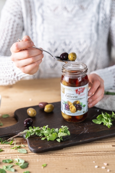 Jemand nimmt Ja! Natürlich Bio-Oliven aus einem Glas.